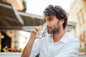 Man with curly hair drinking a glass of water in an upscale urban area